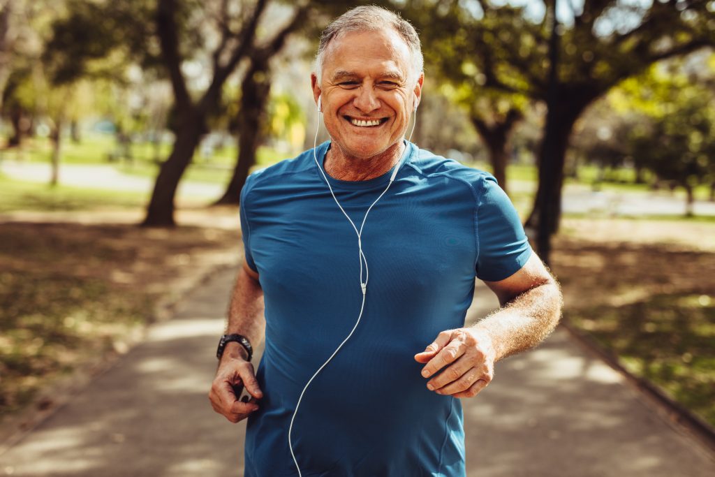 portrait-of-a-senior-man-in-fitness-wear-running-in-a-park-close-up-of-a-smiling-man-running-while-1328442068